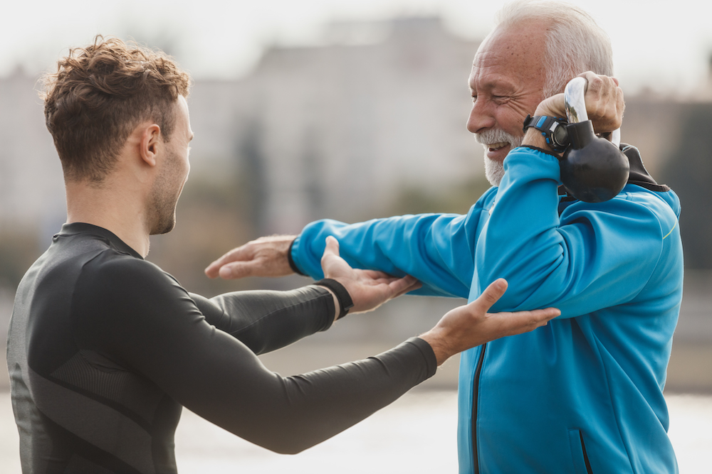 older guy training kettlebell shoulder press with trainer Older male client with personal trainer